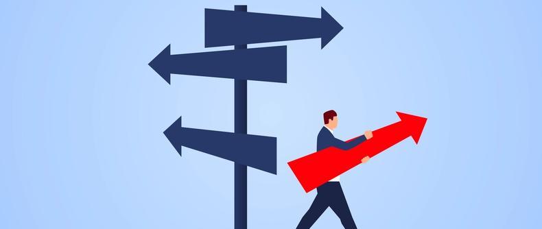 An illustration of a businessman carrying a large red arrow walks past a signpost with multiple direction arrows.